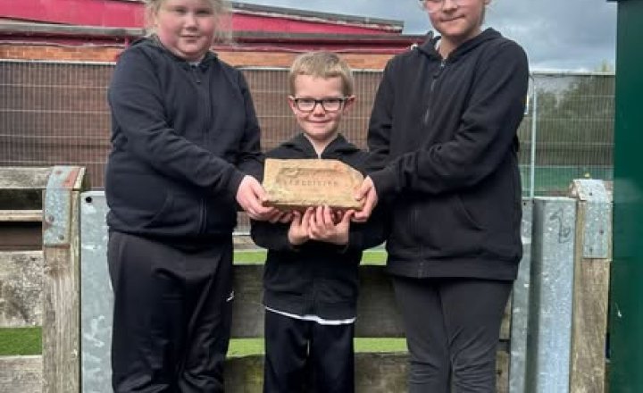 pic of three pupils holding one of the bricks discovered