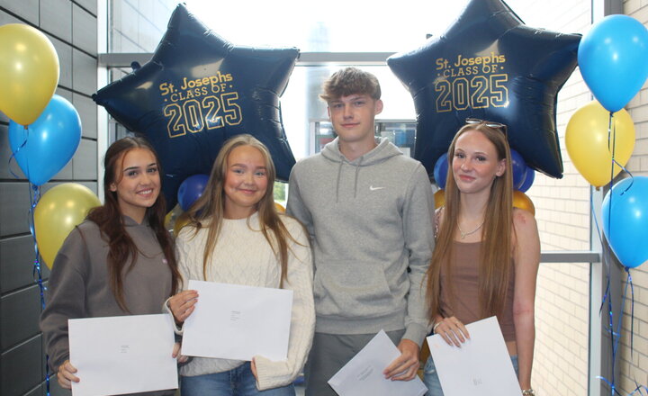 three teenage girls and one boy in front of celebration balloons smiling
