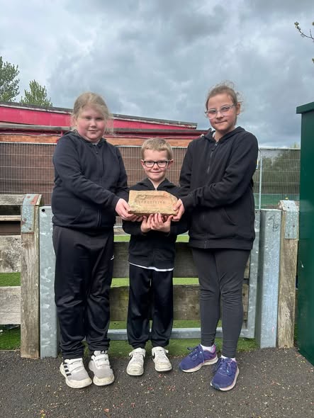 pic of three pupils holding one of the bricks discovered