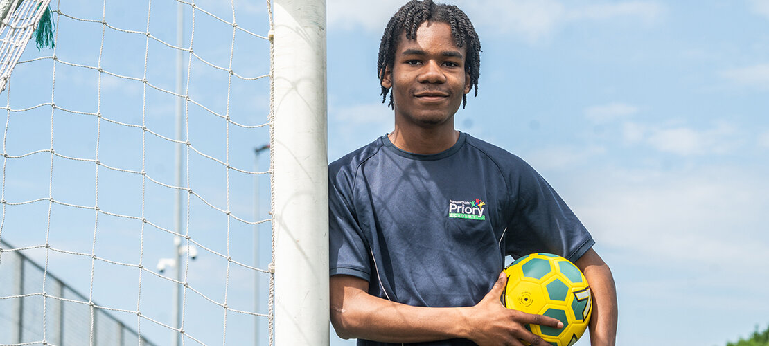 boy in PE kit against goal posts with football under his arm