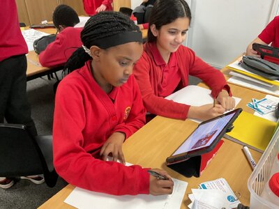 Children writing and using an iPad for research.