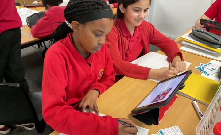 Children writing and using an iPad for research.