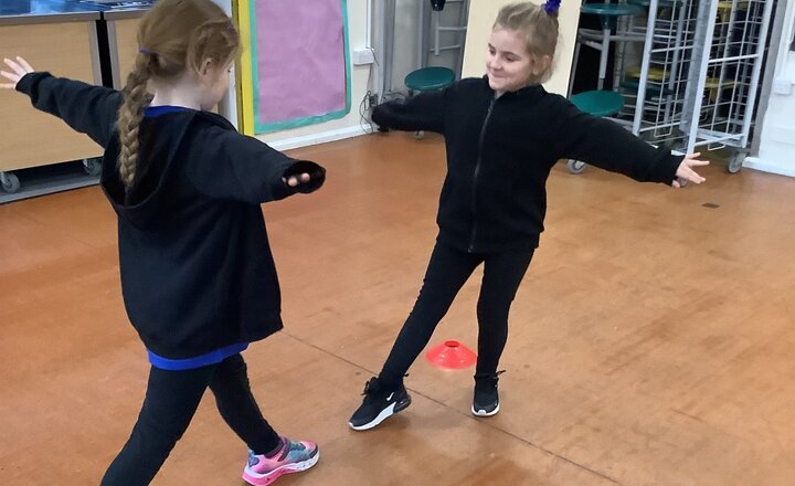 Two St. Bega's pupils in the school hall practising a gymnastics balance activity, standing opposite each other with arms stretched out and feet apart as they mirror each other’s shapes