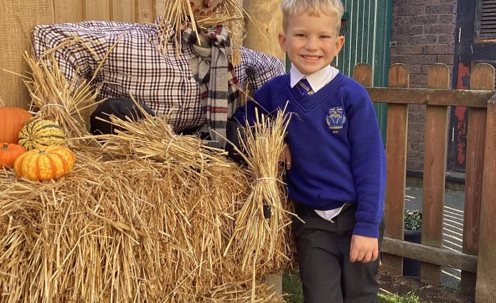 Early Years pupil taking their photo next to Stan the Scarecrow