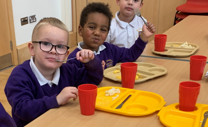 Three boys eating the school dinner, smiling at the camera