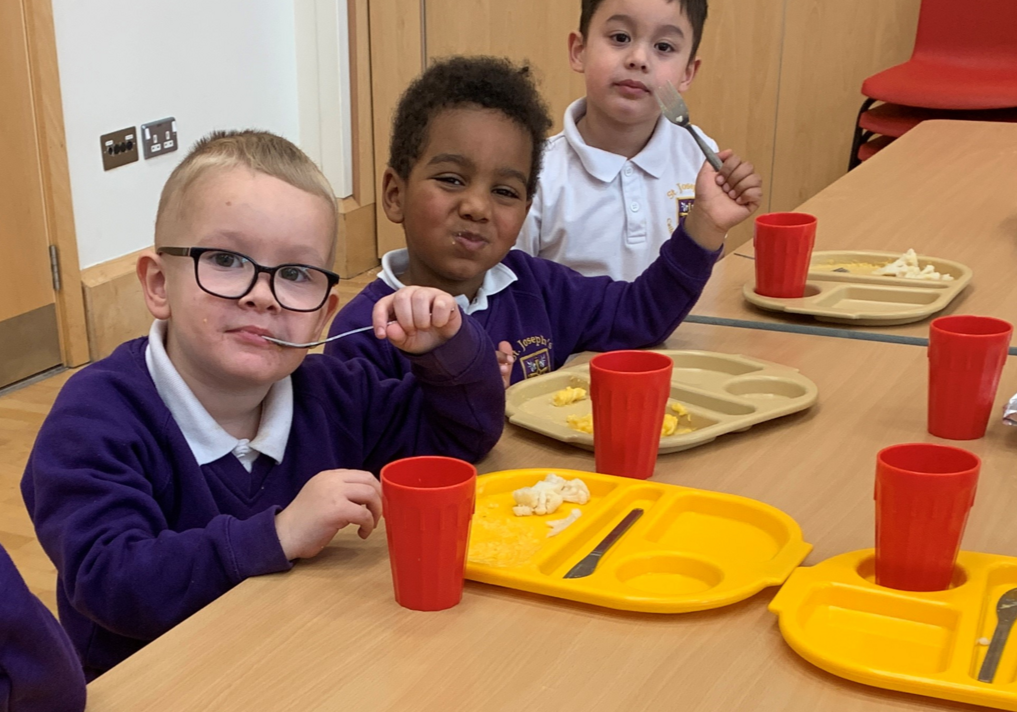 Three boys eating the school dinner, smiling at the camera